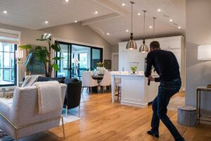 A young couple reviews a home checklist while touring a sunlit living room with large windows.